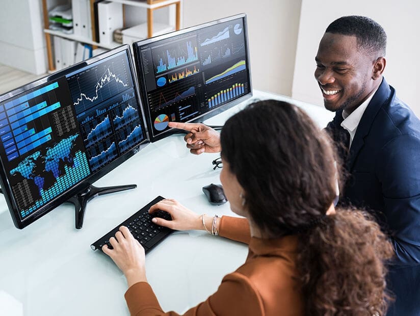 man and woman analyzing dashboards on twin monitors